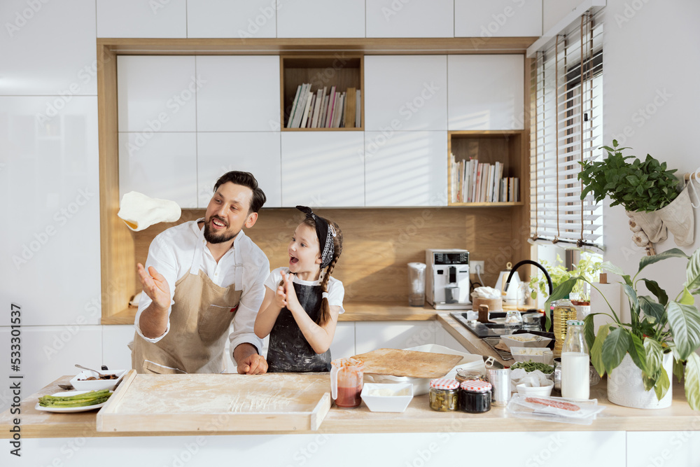 Happy father throwing up homemade dough teaching daughter rolling with hands. Happy curious daughter watching process clapping in hands delightfully. Adorable family cooking baking piza at home. Happy father throwing up homemade dough teaching daughter rolling with hands. Happy curious daughter watching process clapping in hands delightfully. Adorable family cooking baking piza at home.