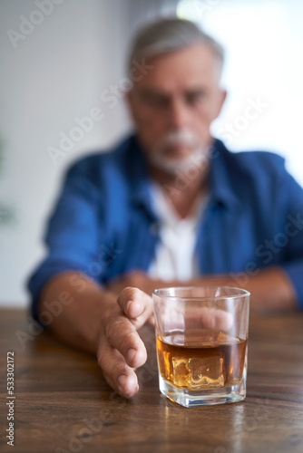 Close up of glass full of whisky and man in background who taking it