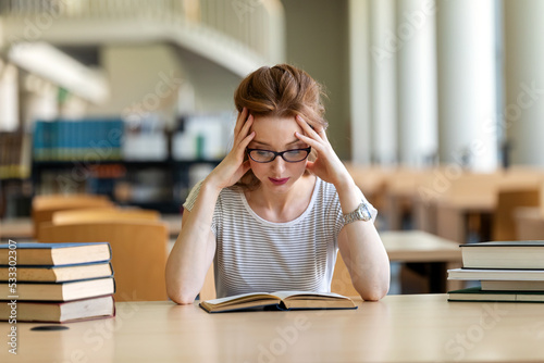 Exhausted young female studying and preparing for exam in college library. Education people concept