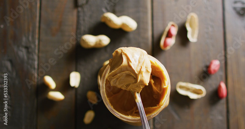 Image of close up of peanut butter and peanuts on wooden background
