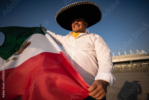 Smiling man wearing sombrero holding Mexican flag on sunny day photo