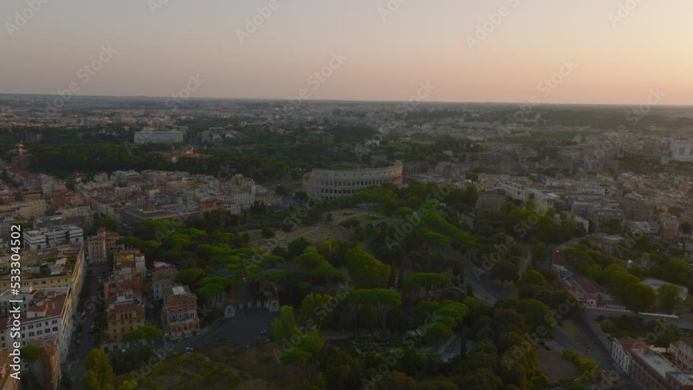 Forwards fly above Oppian Hill park with historic landmarks. Heading towards ancient Colosseum amphitheatre. Panoramic view of city at dusk. Rome, Italy Forwards fly above Oppian Hill park with historic landmarks. Heading towards ancient Colosseum amphitheatre. Panoramic view of city at dusk. Rome, Italy