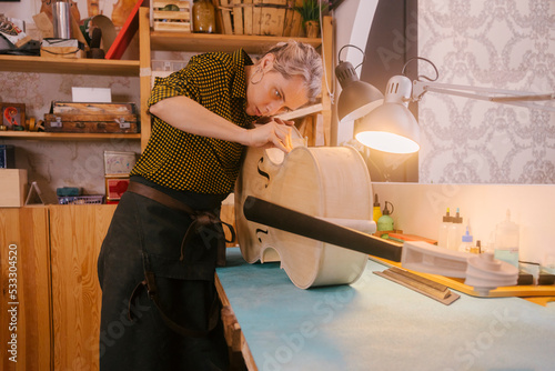 Instrument maker with hand tool working on double bass at workshop photo