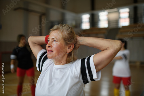 Senior woman stretching before basketball match in gym.