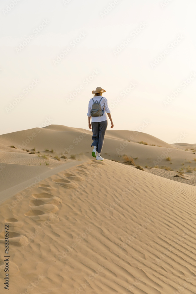 Woman wearing hat walking on sand dunes in desert Woman wearing hat walking on sand dunes in desert
