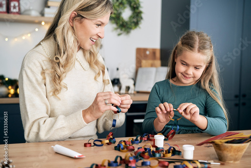 Caucasian girl and mother preparing DIY paper chain for Christmas tree and talking