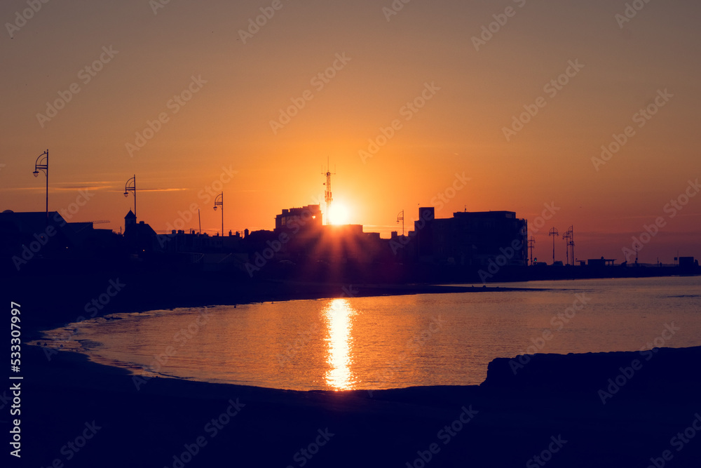 Silhouette of a town buildings by the ocean at sunrise. Warm orange color. Galway city, Ireland. Calm and peaceful mood.
