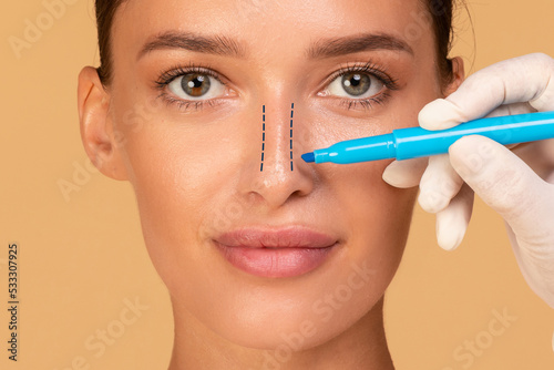 Rhinoplasty concept. Young woman with marking on her nose on beige studio background, closeup photo