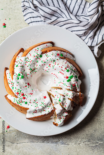 Christmas dessert. Vanilla pound cake with sugar icing and festive colored sprinkles on white plate, gray background.