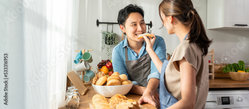 Asian young female holding bread and giving to male in kitchen room.