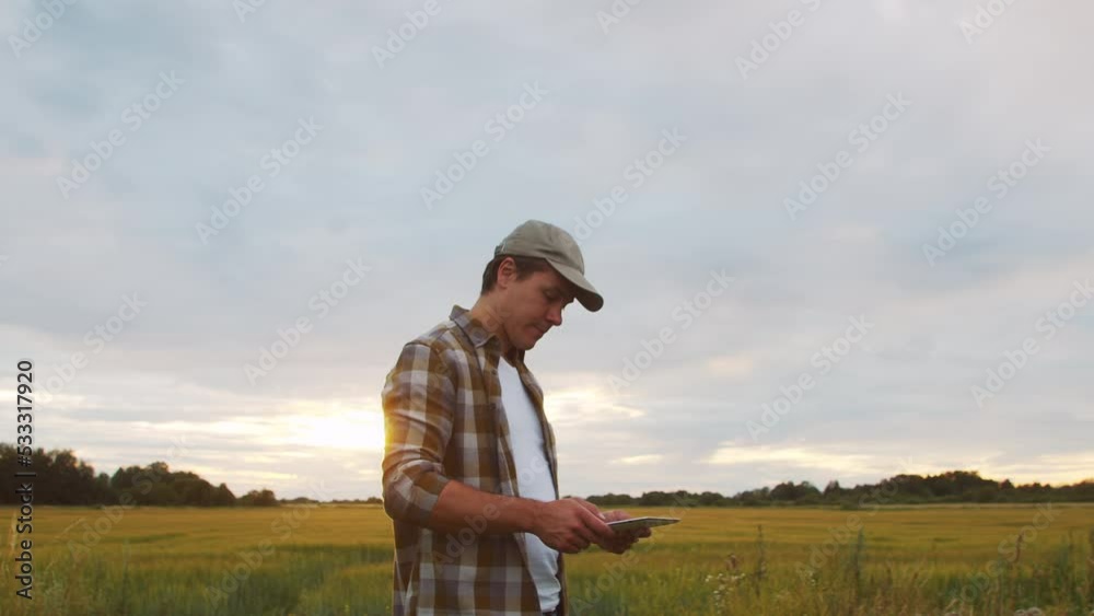 Farmer with a tablet computer in front of a sunset agricultural landscape. Man in a countryside field. Country life, food production, farming and technology concept. Farmer with a tablet computer in front of a sunset agricultural landscape. Man in a countryside field. Country life, food production, farming and technology concept.