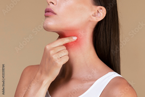 Closeup of unrecognizable sick lady suffering from sore throat, touching neck with hand, inflamed red zone photo