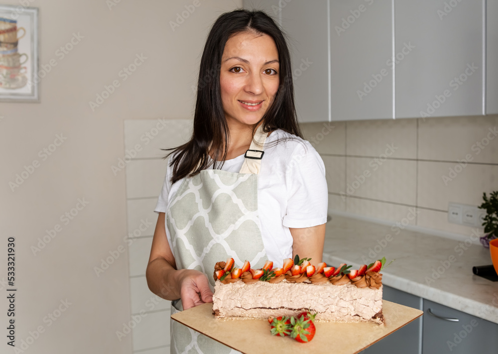 Confectioner decorated with berries a biscuit cake with white cream. Housewife female chef cook confectioner or baker in apron white t-shirt. Cake stands on a table. Homemade pastry, cooking cakes. Confectioner decorated with berries a biscuit cake with white cream. Housewife female chef cook confectioner or baker in apron white t-shirt. Cake stands on a table. Homemade pastry, cooking cakes.