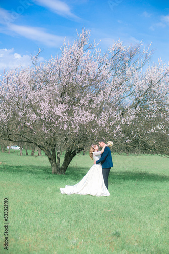 The bride and groom with blond long hair in a white dress in a spring garden near a flowering tree. Emotions and feelings