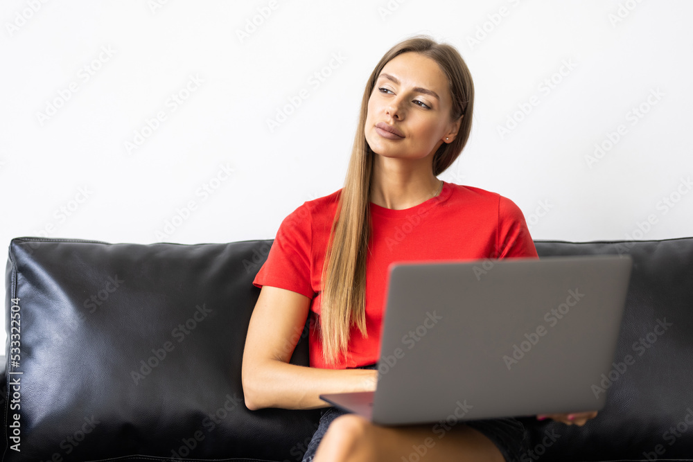 Smiling young woman using laptop, sitting on couch at home Smiling young woman using laptop, sitting on couch at home