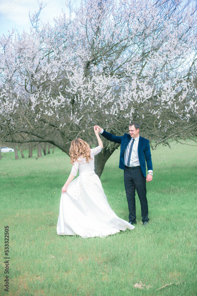 The bride and groom with blond long hair in a white dress in a spring garden near a flowering tree. Emotions and feelings