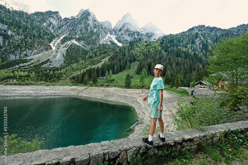 Naklejka premium Boy stand against lake and mountains at Vorderer Gosausee, Gosau, Upper Austria.
