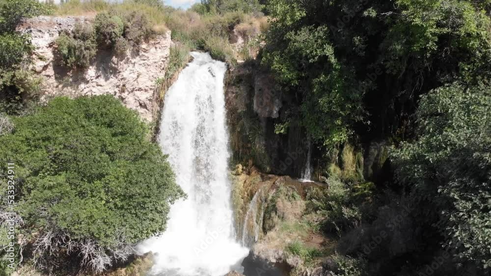 Wild waterfall flowing from rocky ledge surrounded by trees and creates rainbow