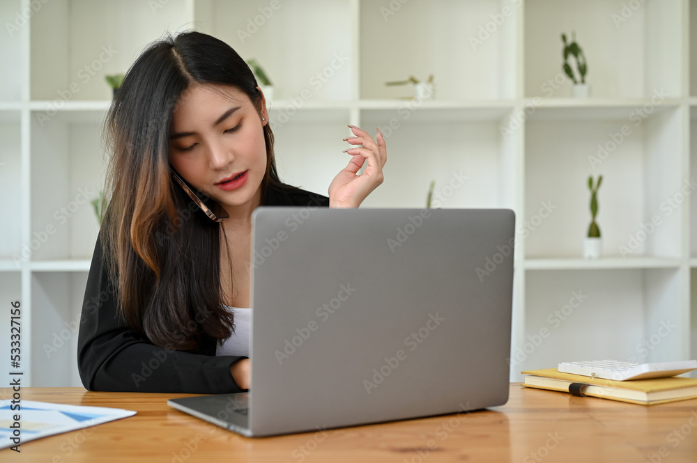 Professional and busy young Asian businesswoman on the phone call with her business client Professional and busy young Asian businesswoman on the phone call with her business client
