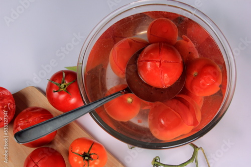 a lot of blanched tomatoes in a bowl with water, ready for peeling photo