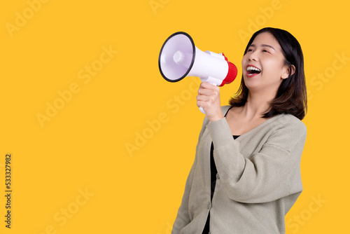 Side view of Asian woman screaming in megaphone, price reduction announcement standing isolated on yellow background. She was excited and happy.