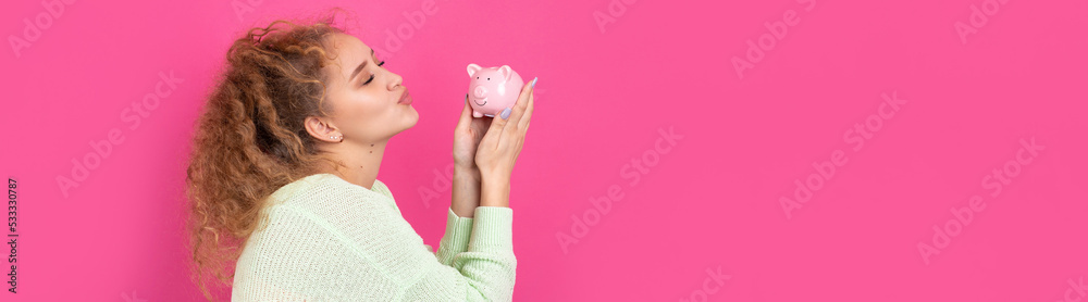 A cute young girl with curly red hair holds a piggy bank, a pink piglet in her hands. The concept of wealth and safety of money. A cute young girl with curly red hair holds a piggy bank, a pink piglet in her hands. The concept of wealth and safety of money.