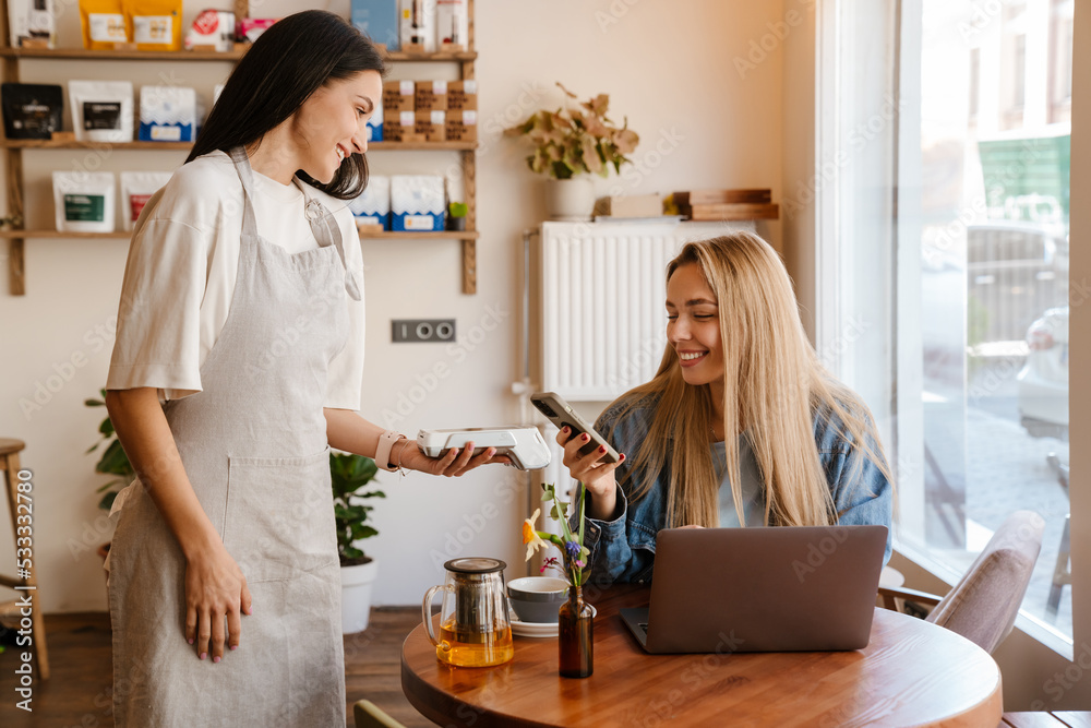 White blonde woman smiling while using cellphone for payment in cafe White blonde woman smiling while using cellphone for payment in cafe