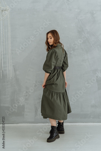 beautiful woman model in a green long dress and rough black boots on a gray background. fashionable women's clothing 2022-2023.