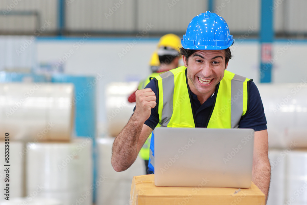 Architect or engineering man and worker standing and checking large warehouse with computer. Caucasian business manager raising hand with exciting emotion and warehouse building background.