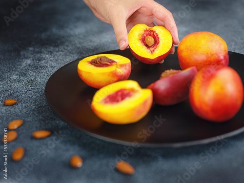 Hand holding fresh peach fruit and black dish with peaches and cloth on table blurred background. Top view. Close-up photo. Healthy food and fruit concept