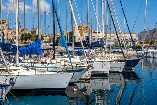 boats and yachts on pier in marine city port with masts and bulidings and blue sky on background