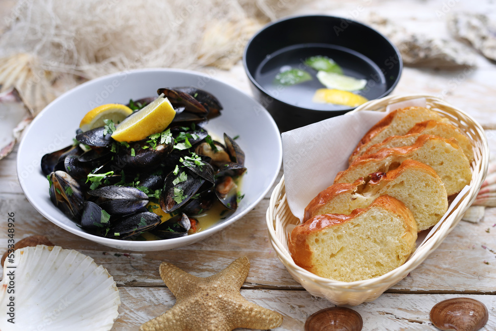 Mussels in wine-butter sauce, sprinkled with parsley, served with bread. Clams in a bowl, on white wood background. Mussels in wine-butter sauce, sprinkled with parsley, served with bread. Clams in a bowl, on white wood background.