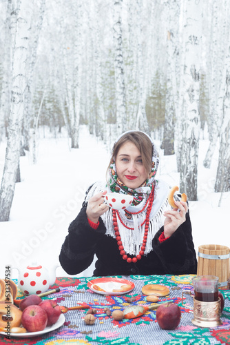 A girl in a winter forest. A beautiful woman in a fur coat at a covered table among the birches