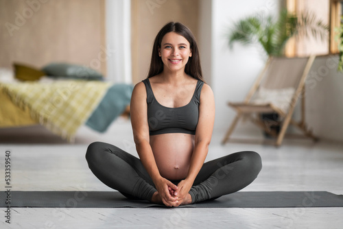 Pregnant Woman In Activewear Sitting On Yoga Mat And Smiling At Camera