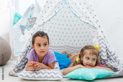 childhood and hygge concept - happy little girls playing in kids tent