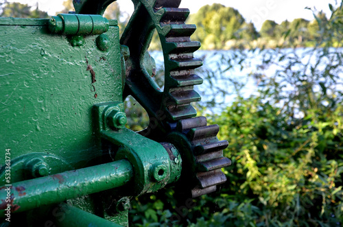 don't stick your fingers where you don't belong. eyelessness when working with gears that fit together. green wheels of the embankment drive by the river. very old pond sluice gate painted green photo