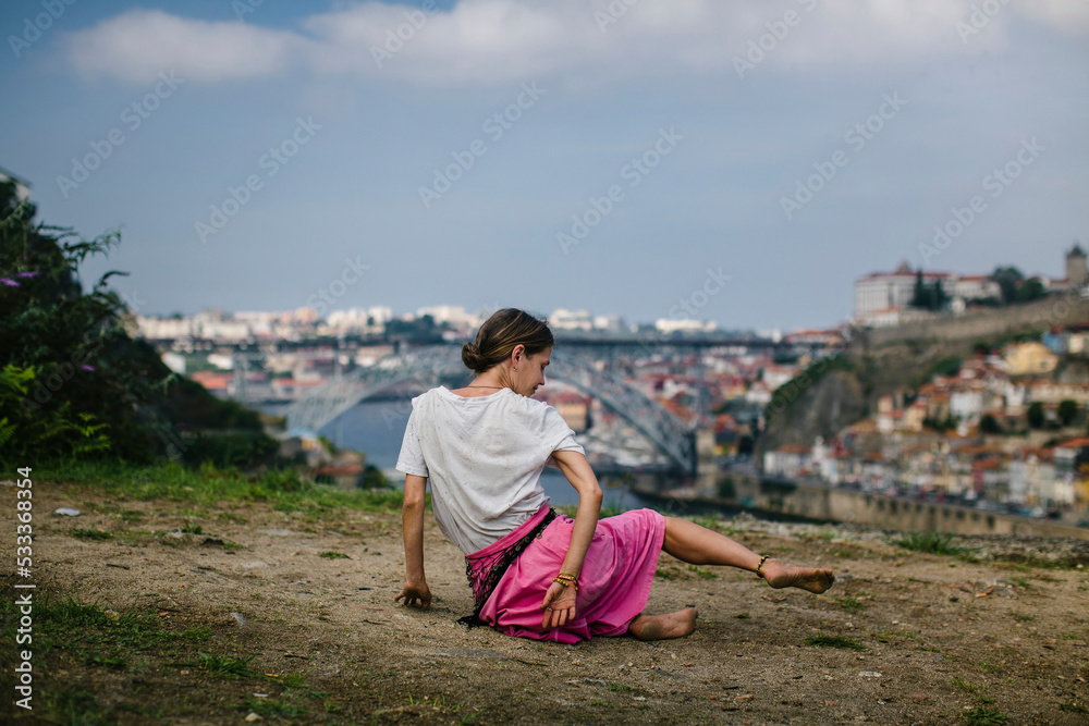 A woman dances on the banks of the Douro River in front of the Dom Luis Bridge, Porto, Portugal.