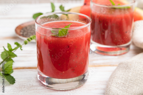 Watermelon juice with chia seeds and mint in glass on a white wooden background with linen textile. Side view.