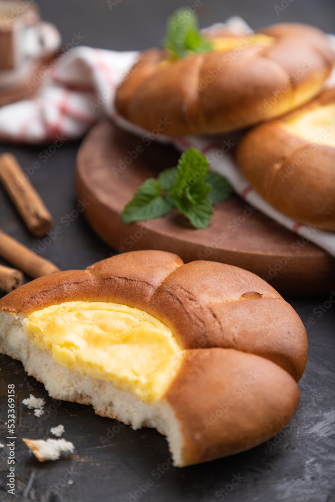 Sour cream bun with cup of coffee on a black concrete background. Side view, close up, selective focus. Sour cream bun with cup of coffee on a black concrete background. Side view, close up, selective focus.