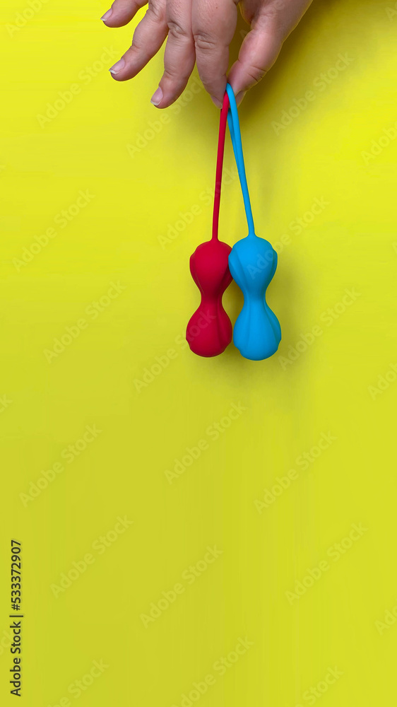 Sex toys. Red and blue geisha balls on a hand. Yellow background. Useful for sex shop, adult Sex toys. Red and blue geisha balls on a hand. Yellow background. Useful for sex shop, adult