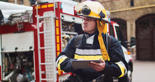 Portrait of fireman in helmet and gull equipment viewing on sides and writting data to tablet. Rescuer working with latest technologies. The concept of saving lives, heroic profession, fire safety photo