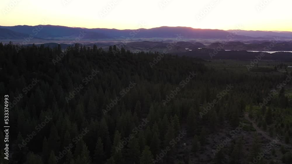 An aerial shot of over a dark forest with the sun behind the distant pink and blue lit mountains. An aerial shot of over a dark forest with the sun behind the distant pink and blue lit mountains.
