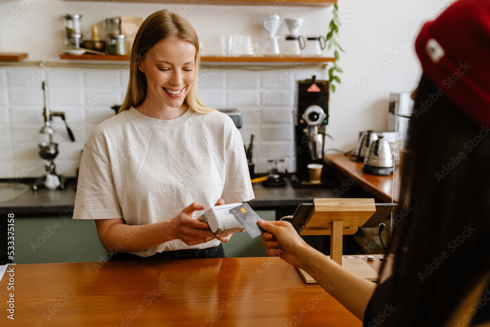 Blonde white barista woman working with terminal in cafe