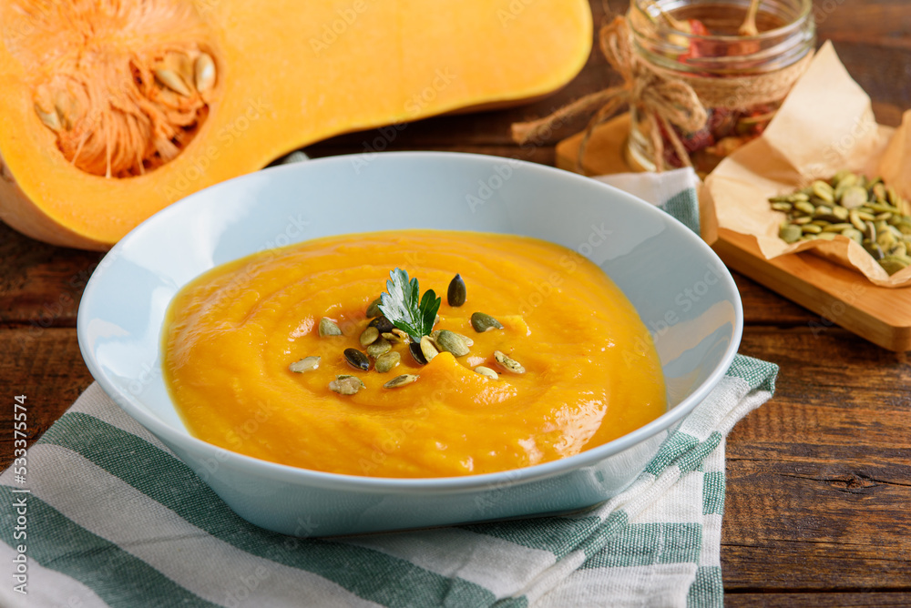 pumpkin soup in blue plate on wooden table decorated with pumpkin seeds and parsley, autumn seasonal recipes pumpkin soup in blue plate on wooden table decorated with pumpkin seeds and parsley, autumn seasonal recipes