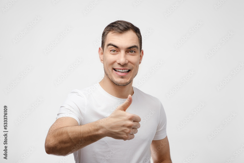 portrait of smiling brunette man in white clean T-shirt on white background shows thumbs up, super. for advertising portrait of smiling brunette man in white clean T-shirt on white background shows thumbs up, super. for advertising