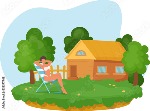 Beautiful woman in swimsuit resting on deckchair in backyard. Attractive girl sunbathing on green lawn in front of wooden cottage. Girl enjoying summer relaxing on nature