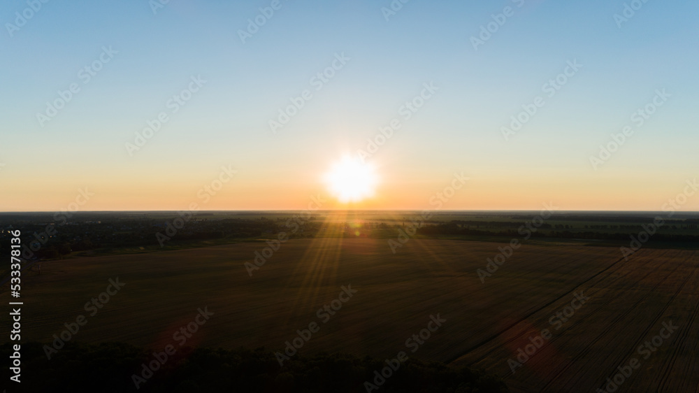 Aerial view over a wheat field during sunset. Drone flies over agricultural wheat field during sunrise. Drone shot beautiful summer landscape of a wheat field, sun and sky