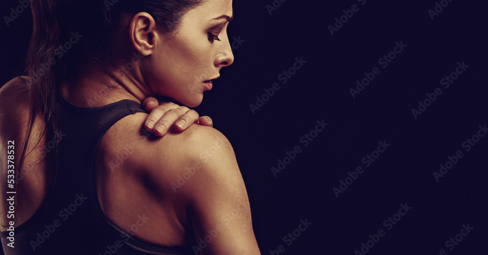 Strong sporty woman doing hands the massege to relax the tension in shoulder and scapula in sport bra top on empty copy space black studio background. Sports injury. Closeup toned portrait. Back view. Strong sporty woman doing hands the massege to relax the tension in shoulder and scapula in sport bra top on empty copy space black studio background. Sports injury. Closeup toned portrait. Back view.
