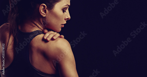Strong sporty woman doing hands the massege to relax the tension in shoulder and scapula in sport bra top on empty copy space black studio background. Sports injury. Closeup toned portrait. Back view.