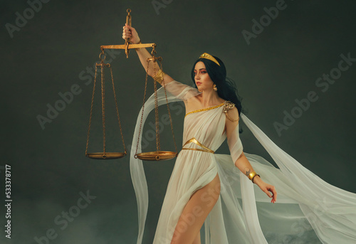 Portrait fantasy woman Greek goddess of justice Themis, holding golden scales in hands. White silk vintage dress old antique style flies waving in wind. Girl sexy Virgo astrology zodiac sign art photo